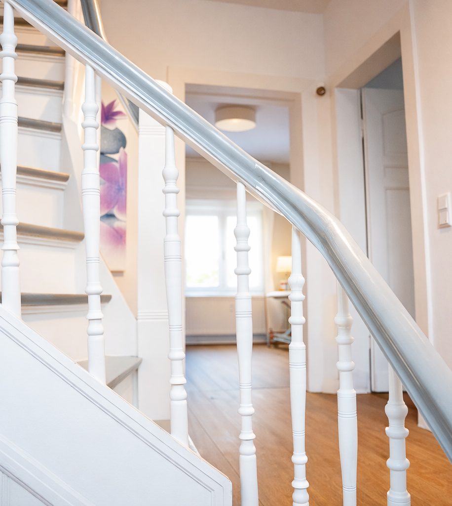 Helle Treppe mit weißen Geländern, Blick auf einen lichtdurchfluteten Raum.